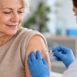Femme senior recevant un vaccin dans le bras par un professionnel de santé, dans un cabinet médical lumineux.